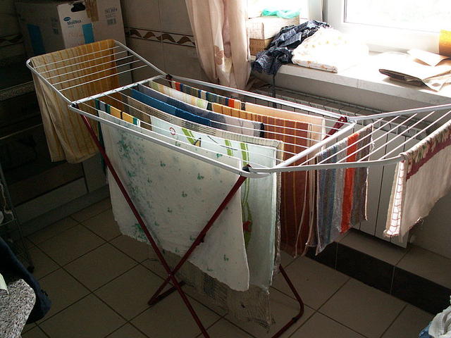 A silver foldable drying rack inside a living room with many types of clothing hand drying